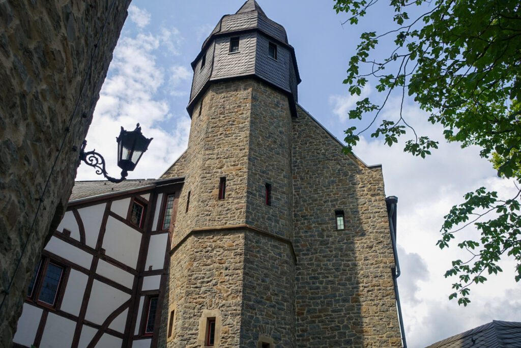 A close up picture of the architecture of Burg Altena, a medieval castle in Altena, Germany. The sky is blue and contrasts to the sandstone coloured brick of the castle. The traditional styling of German half timbered houses is reflected in the architecture of the castle.