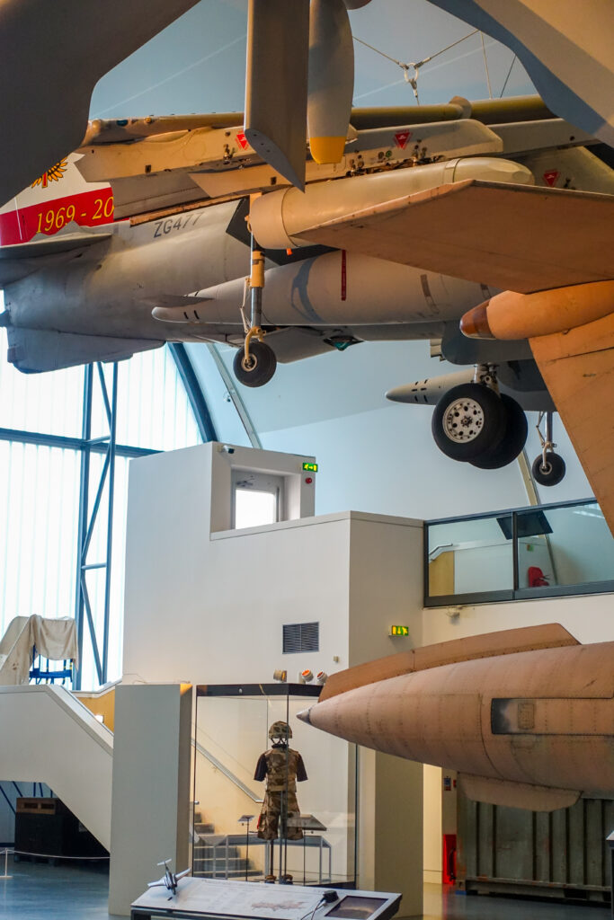 An interior view of one of the largest hangars at the RAF Museum in London. The room is multi story and there are planes suspended in the air as well as on the ground floor of the exhibition hall.