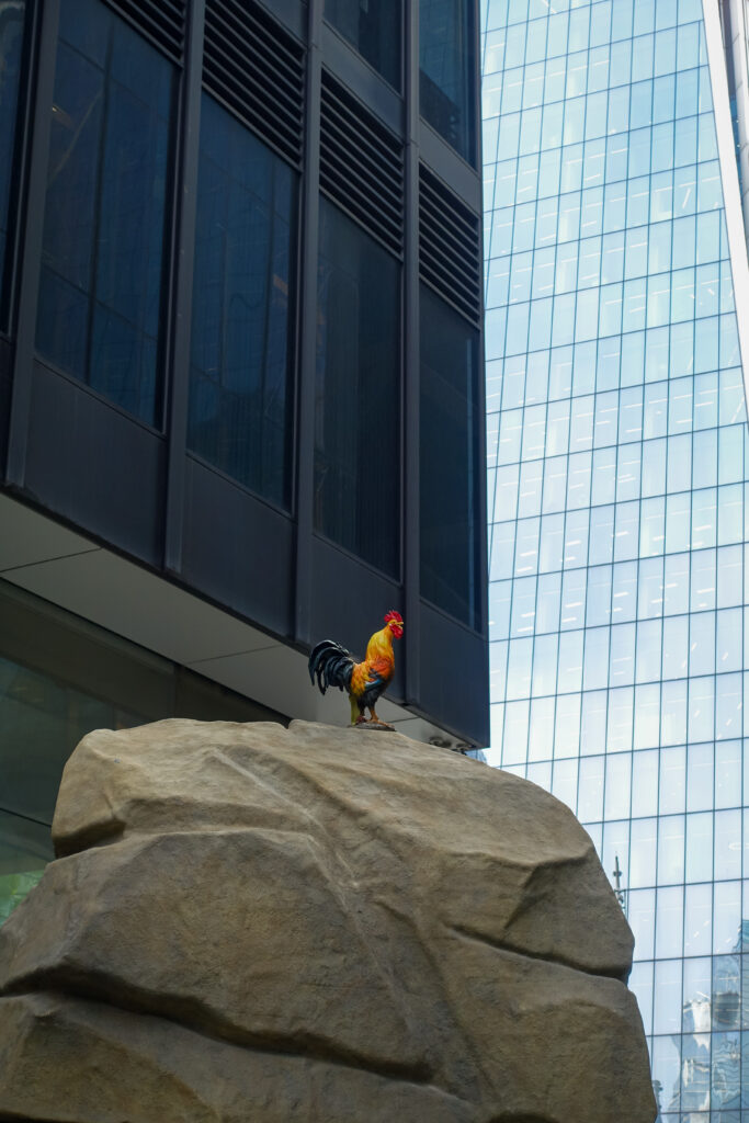 A picture of Horizon 22, infront of the glass skyscraper is a hen sitting on a rock. The hen is coloured orange, red and blue. The skyscraper is one of the tallest in London and offers London's tallest viewing platform.
