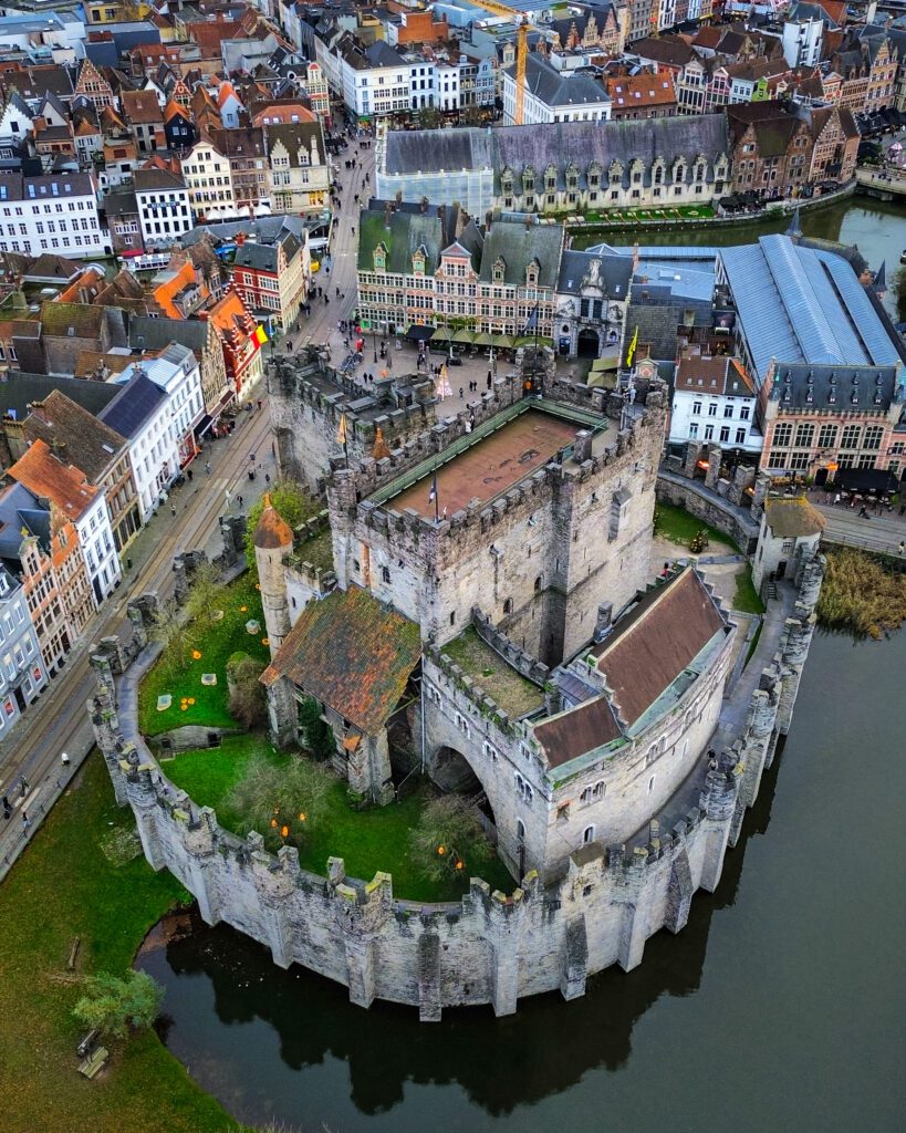 An aerial view of the 12th century medieval castle Gravensteen in Ghent. Surrounding the castle is a moat and you can see the fairy-tale facades of the buildings surrounding the castle.