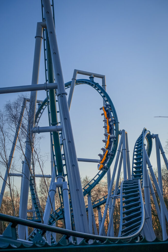 The yellow train of the emerald green rollercoaster fønix at fårup sommerland races around the track through multiple inversions against a backdrop of Danish sunsets.