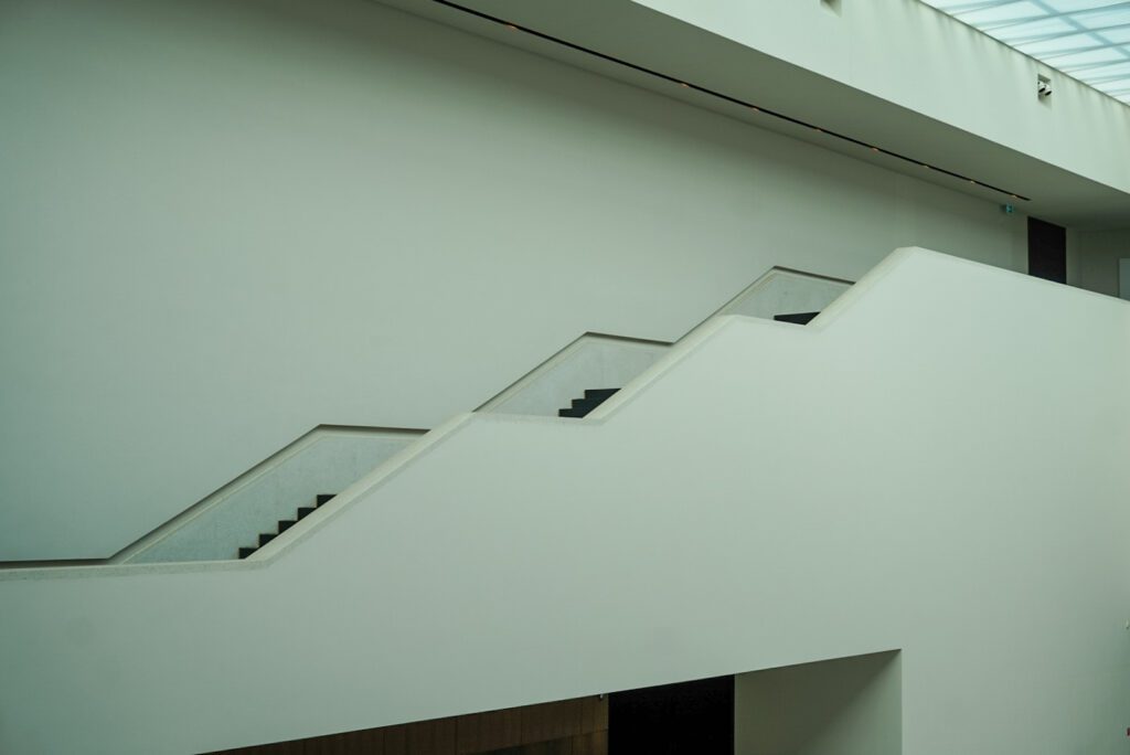 The staircase of the LWL Museum is one of the most-magnificent architectural masterpieces of the entire building. The staircase zig-zags from the ceiling, which is made up of glass roof-tiling, down to the ground. The walls of the foyer are white and match the white railing of the staircase.