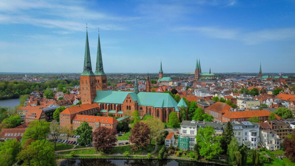 One of seven spires in the city of Lübeck is the city's cathedral - the Lübecker Dom. The cathedral is constructed out of red brick, with green spires. It's situated directly behind the Mühlenteich. In the background , you can spot a number of other spires in the city, all of which have green roof-tiling.